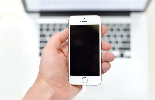 Person holding an iPhone in front of a MacBook Person holding an iPhone in front of a MacBook